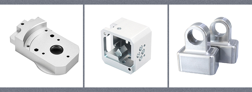 Three precision-machined aluminum alloy parts: a block with holes, a box with internal features, and two connected hooks