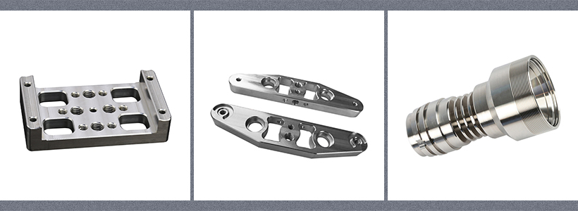 Three machined stainless steel parts: a rectangular plate with holes, two long L-shaped brackets, and a cylindrical part with grooves.