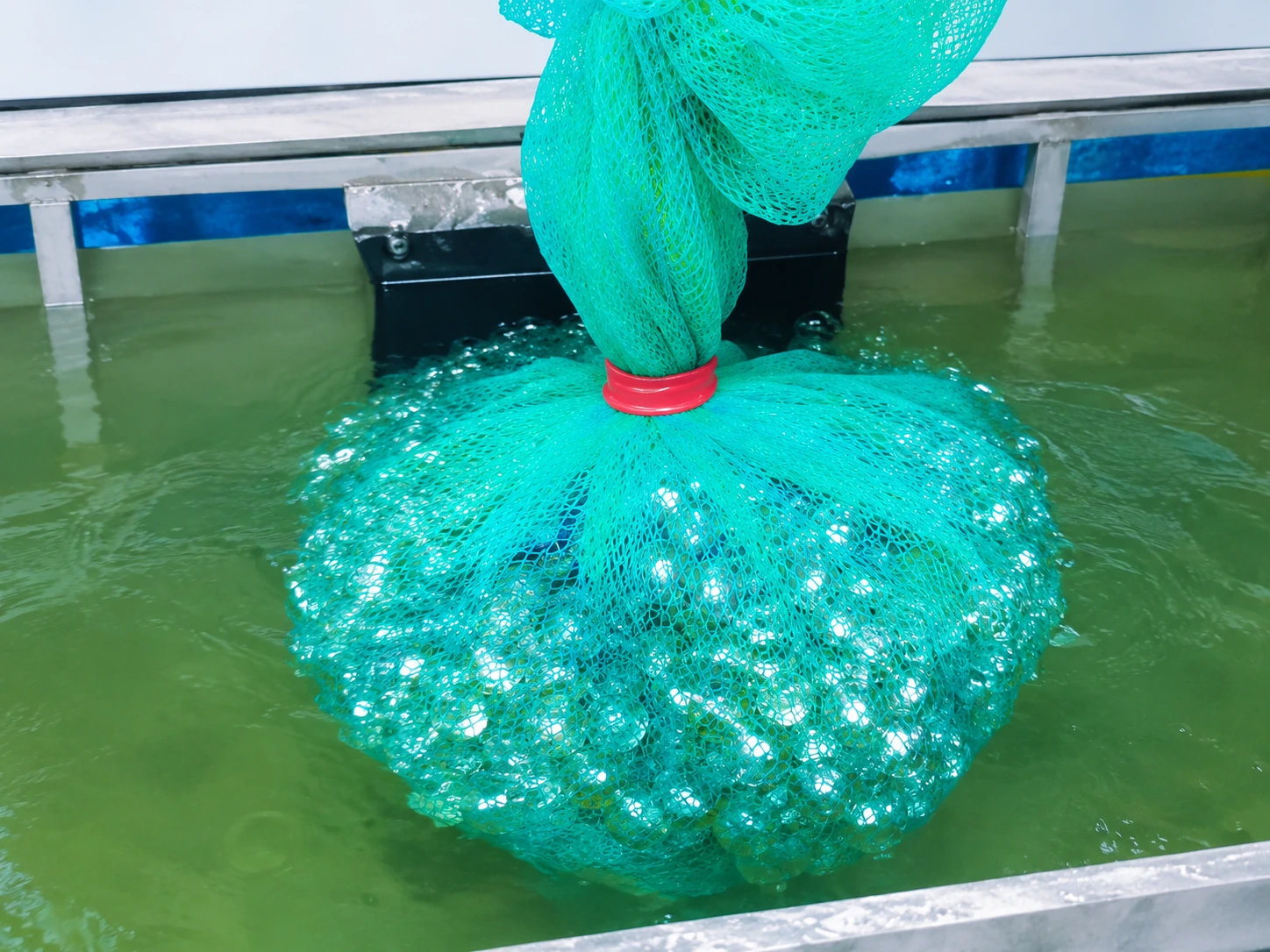 Close-up of mesh bag containing small aluminum parts submerged in anodizing bath solution